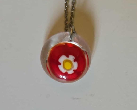 Necklace with a red pendant featuring a white flower design on a plain background