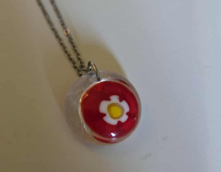 Necklace with a red pendant featuring a white flower design on a light gray background